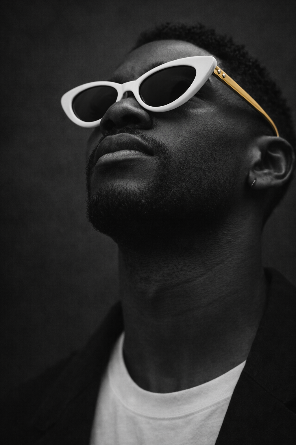Man wearing white sunglasses with gold accents against a dark background